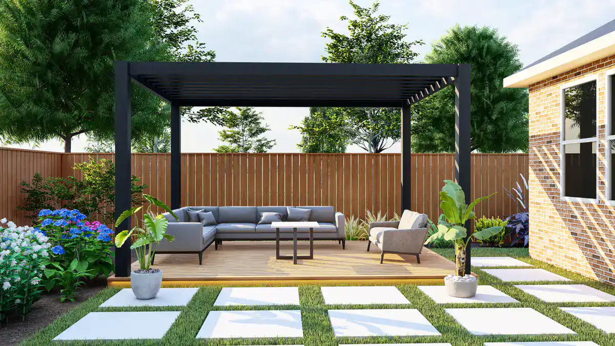 A modern backyard with a pergola over a patio, featuring outdoor furniture, potted plants, and a wooden fence. The patio is bordered by grass and stone pavers, with trees and flowering shrubs in the background.