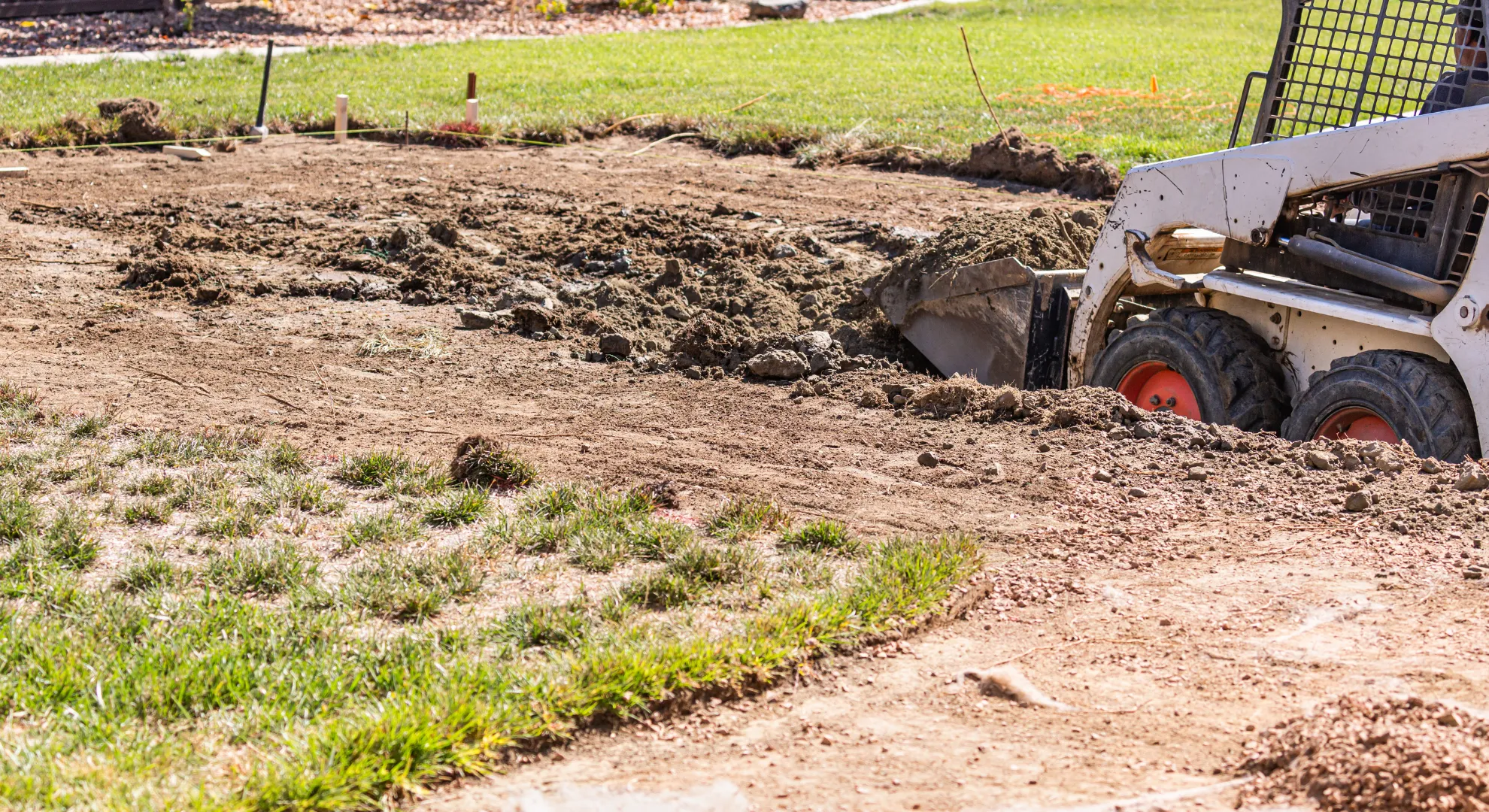 A small bulldozer levels a yard, moving dirt across soil and grass for landscaping and construction projects.