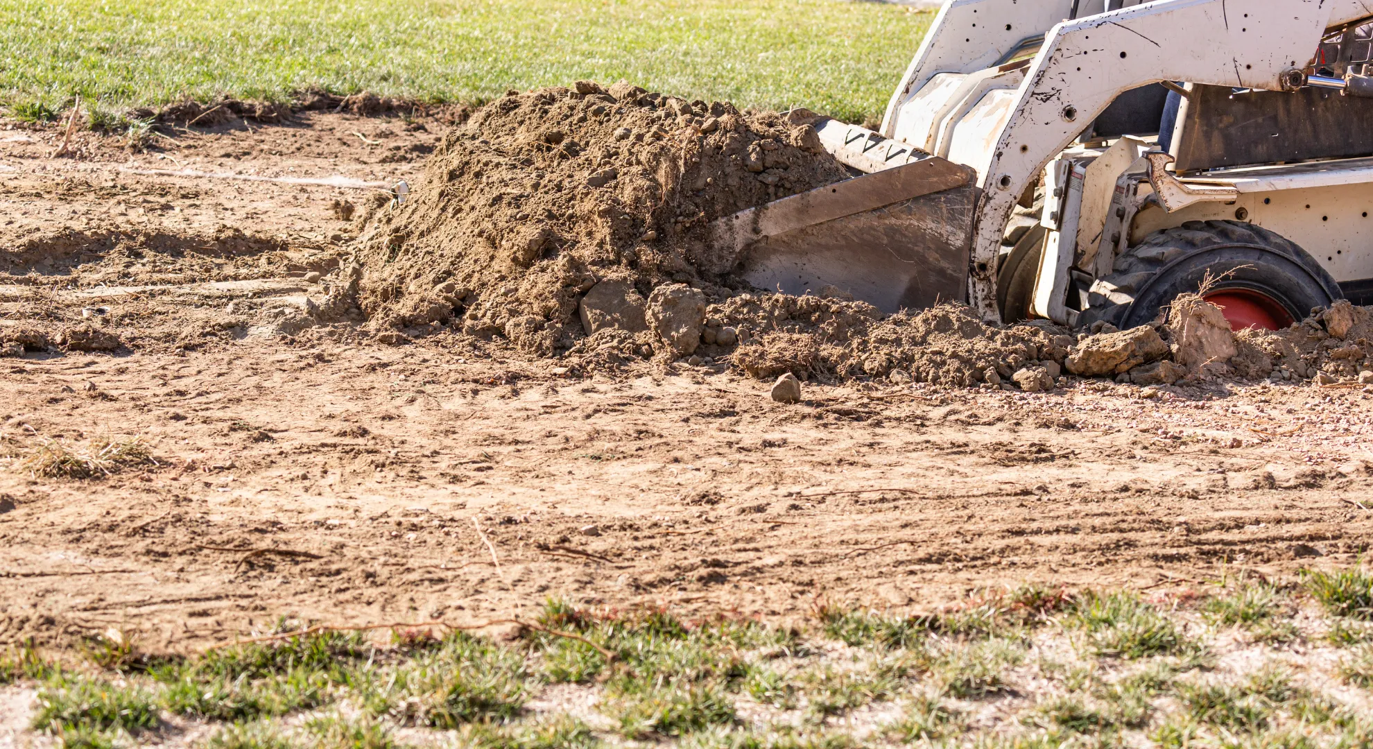 A small bulldozer pushes dirt on a lawn, leveling ground in preparation for new landscaping work.